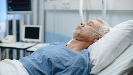 Obraz premium In the Hospital Sick Man Rests, Lying on the Bed. Recovering Man Sleeping in the Modern Hospital Ward.