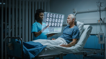 In the Hospital, Senior Patient Lying in the Bed Nurse Holding Tablet Computer Shows Augmented Reality Information about Brain Scans and Medical History. In the Technologically Advanced Hospital Ward.