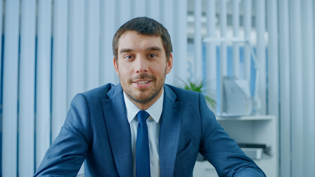 Handsome Respectable Businessman Sitting At His Desk In Office, Looking Into The Camera.