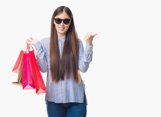 Young Chinese woman over isolated background holding shopping bags on sales pointing and showing with thumb up to the side with happy face smiling