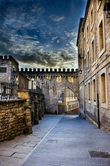 High dynamic range photograph of a street in the old part of Vitoria, Spain, with part of a crenellated wall and its raked door, cobblestone floor and granite stone facades