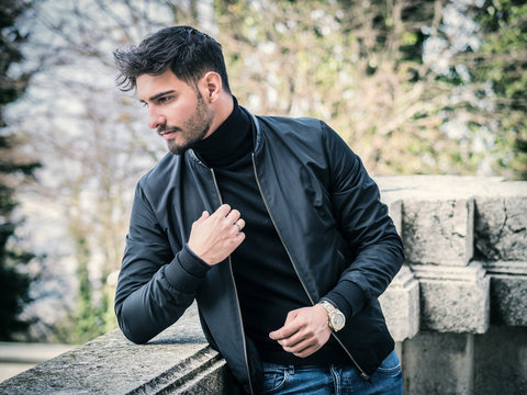 One handsome young man in urban setting in city, wearing black leather jacket and jeans