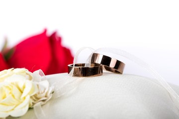 golden wedding rings - wedding ring on a silk pillow with red roses in the background
