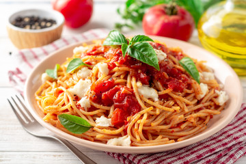 Spaghetti pasta with tomato sauce, mozzarella cheese and fresh basil in plate on white wooden...