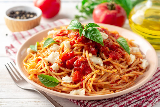 Spaghetti pasta with tomato sauce, mozzarella cheese and fresh basil in plate on white wooden background. Selective focus.