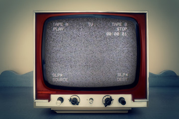 A retro vintage TV showing a VCR double deck tracking an empty noisy VHS tape screen.
