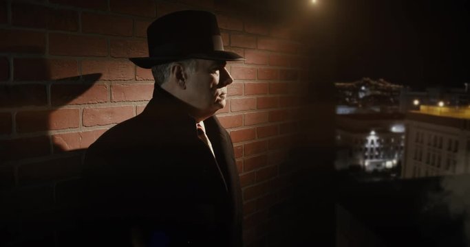 A classic film noir 1940s style scene with a suspicious character wearing a fedora standing in the shadows of a dimly lit rooftop who checks the time on his wristwatch.