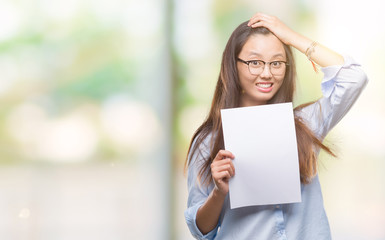 Young asian woman holding blank paper over isolated background stressed with hand on head, shocked with shame and surprise face, angry and frustrated. Fear and upset for mistake.
