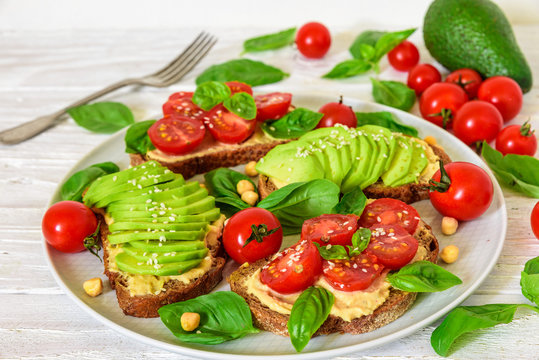 healthy avocado and tomatoes sandwiches with hummus, sesame and basil in a plate with fork