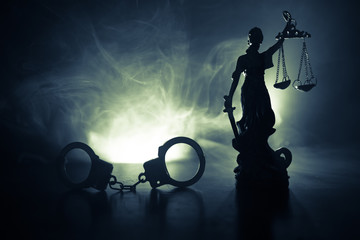 Legal law concept. Silhouette of handcuffs with The Statue of Justice on backside with the flashing red and blue police lights at foggy background.