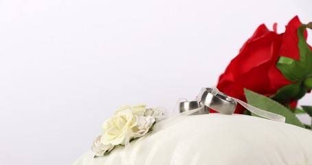 wedding rings - wedding rings on a white silk pillow with red roses in the background