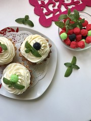 A cake basket with cream and berries and mint leaves. Nearby is a container with berries of different colors for decoration.