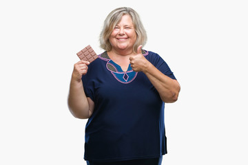 Obraz premium Senior plus size caucasian woman eating chocolate bar over isolated background happy with big smile doing ok sign, thumb up with fingers, excellent sign