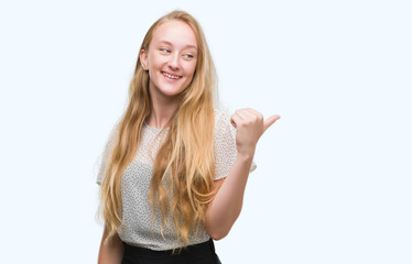 Blonde teenager woman wearing moles shirt smiling with happy face looking and pointing to the side with thumb up.