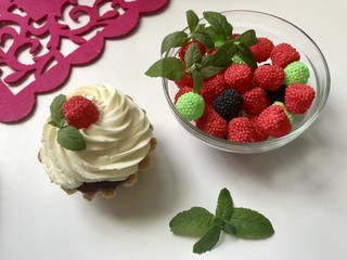 A cake basket with cream and berries and mint leaves. Nearby is a container with berries of different colors for decoration.
