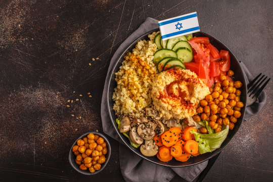Buddha bowl with vegetables, mushrooms, bulgur, hummus and baked chickpeas. Dark background, top view. Israeli food concept.