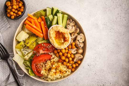 Buddha bowl with vegetables, mushrooms, bulgur, hummus and baked chickpeas. White background, top view.