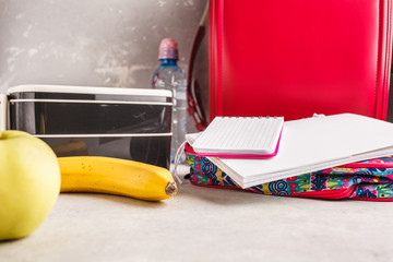 Healthy meal prep containers, notebook and backpack, fruits and water. Takeaway food on white background.