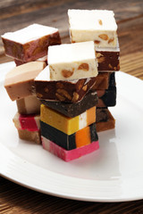 Delicious traditional Italian festive torrone or nougat with nuts on wooden background. Soft nougat blocks with almonds and in diffrent colors. Italian sweets