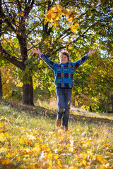 Smiling boy throwing autumn leaves on park