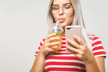 Beautiful young woman drinking a homemade detox juice, texting on her phone while isolated over white. Using phone.