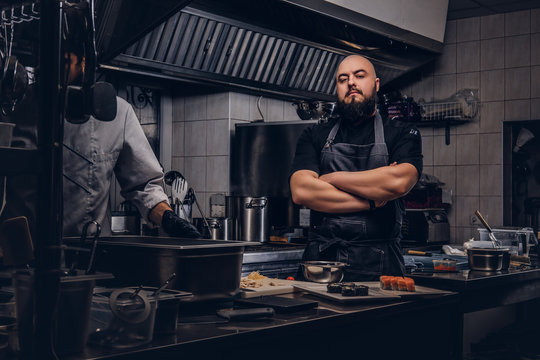 Two brutal cooks dressed in uniforms preparing sushi in a kitchen.
