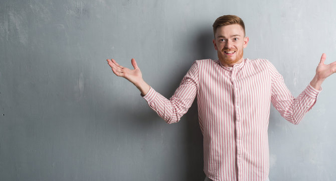 Young redhead man over grey grunge wall very happy and excited, winner expression celebrating victory screaming with big smile and raised hands