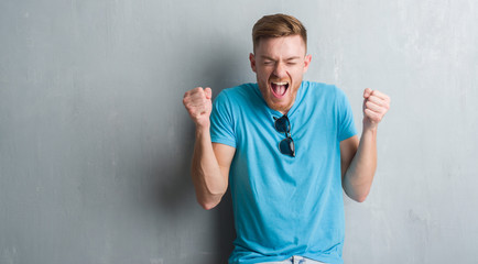 Young redhead man over grey grunge wall wearing casual outfit excited for success with arms raised celebrating victory smiling. Winner concept.