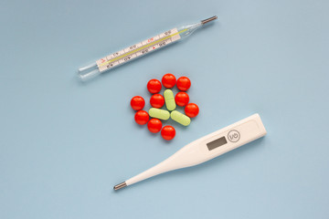 Mercury and electronic thermometer with pills on a blue background