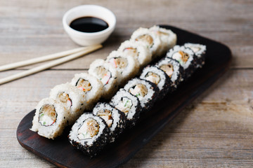 Japanese restaurant menu photo, seafood, national cuisine. Delicious sushi rolls served on wooden tray with sauce and chopsticks