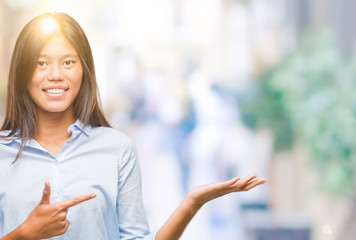 Young asian business woman over isolated background amazed and smiling to the camera while presenting with hand and pointing with finger.
