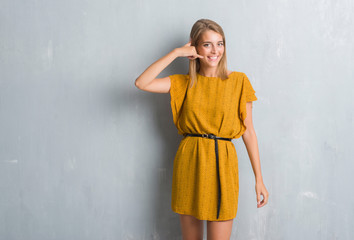 Beautiful young woman standing over grunge grey wall wearing a dress smiling doing phone gesture with hand and fingers like talking on the telephone. Communicating concepts.