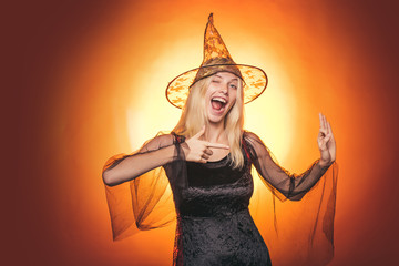 Surprised woman in witches hat and costume on red Halloween background. Beautiful young surprised...