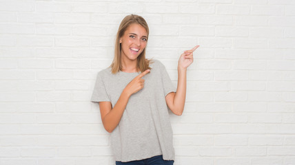 Beautiful young woman over white brick wall smiling and looking at the camera pointing with two hands and fingers to the side.