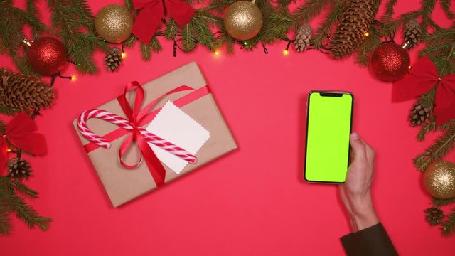 Hand holding smartphone next to gift box on Christmas flatlay