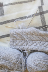 Knitting needles. Fingerless gloves knitted of gray on the background of scarves. Blur, soft focus.