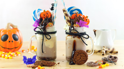 On-trend Happy Halloween theme freak shakes chocolate milkshakes decorated with candy, cookies and lollipops.
