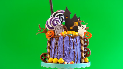 On trend Halloween candyland fantasy novelty drip cake and party table against chroma key green...