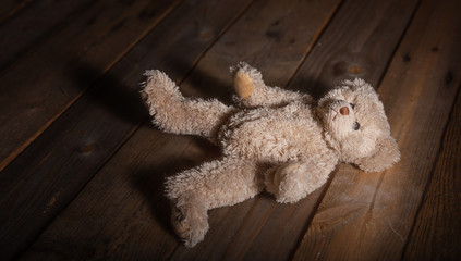 Child abuse. Teddy bear on the floor, dark wooden background