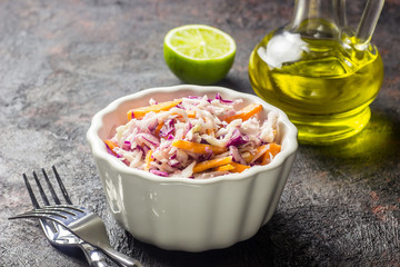 Fresh coleslaw salad made of shredded red and white cabbage and carrots, served in bowl, on dark background