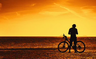 Fototapeta na wymiar Cyclist with bike resting on beach at sunset