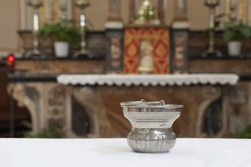 Religious object above white tablecloth an altar in background, slightly out of focus