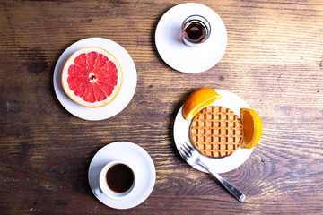 Breakfast With Grapefruit, Coffee, Waffle, Syrup and Orange On Wooden Table With Fork.