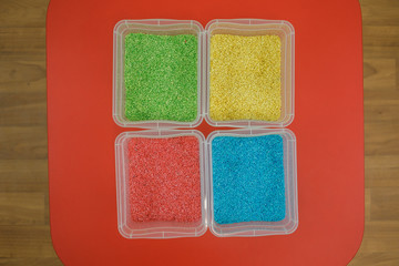 Fototapeta premium Rainbow sensory boxes for toddlers with colourful rice on red table. Universal educational kit in kindergarten.