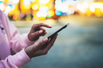 Person pointing finger on screen smartphone on defocus background bokeh light in evening street, hipster girl using in hands mobile phone gadget in night atmospheric city, online wifi internet concept