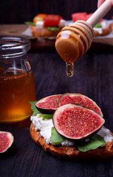 Bruschetta with figs, soft cheese and arugula. Honey is dripping from the spoon