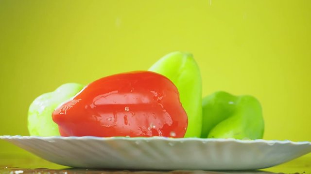 Fresh Balgar peppers fall with water on a plate. The concept of nutrition. Isolate on a yellow background, slowdown.