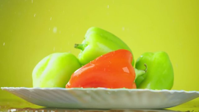 Fresh Balgar peppers fall with water on a plate. The concept of nutrition. Isolate on a yellow background, slowdown.