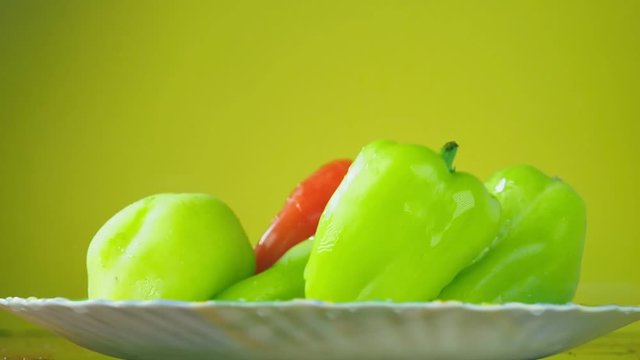 Fresh Balgar peppers fall with water on a plate. The concept of nutrition. Isolate on a yellow background, slowdown.