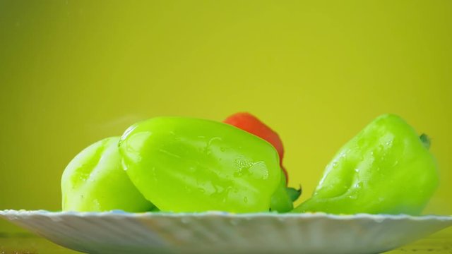 Fresh Balgar peppers fall with water on a plate. The concept of nutrition. Isolate on a yellow background, slowdown.